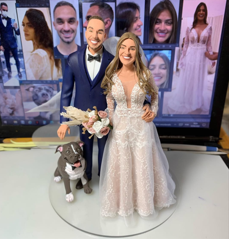 Esculturas de casal de noivos com vestido dourado e smoking azul, acompanhados de escultura de cachorro